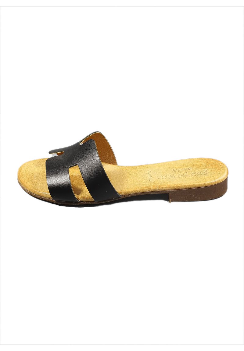 Sandalo scivolato in pelle nera con due cinturini a taglio, soletta imbottita color tan e suola piatta in gomma marrone. Design minimalista.
