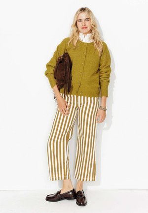 Cardigan en laine vert olive, chemise blanche à col, pantalon large à rayures marron et blanches, sac à main frangé marron et chaussures foncées.