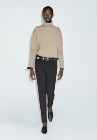 Maglione beige a collo alto, vestibilità rilassata; pantaloni neri aderenti; scarpe nere slip-on. Design semplice con pochi dettagli e texture minime.