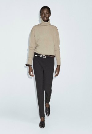 Beiger Rollkragenpullover, lockere Passform; schwarze figurbetonte Hose; schwarze Slipper. Einfaches Design mit minimalen Akzenten und Texturen.