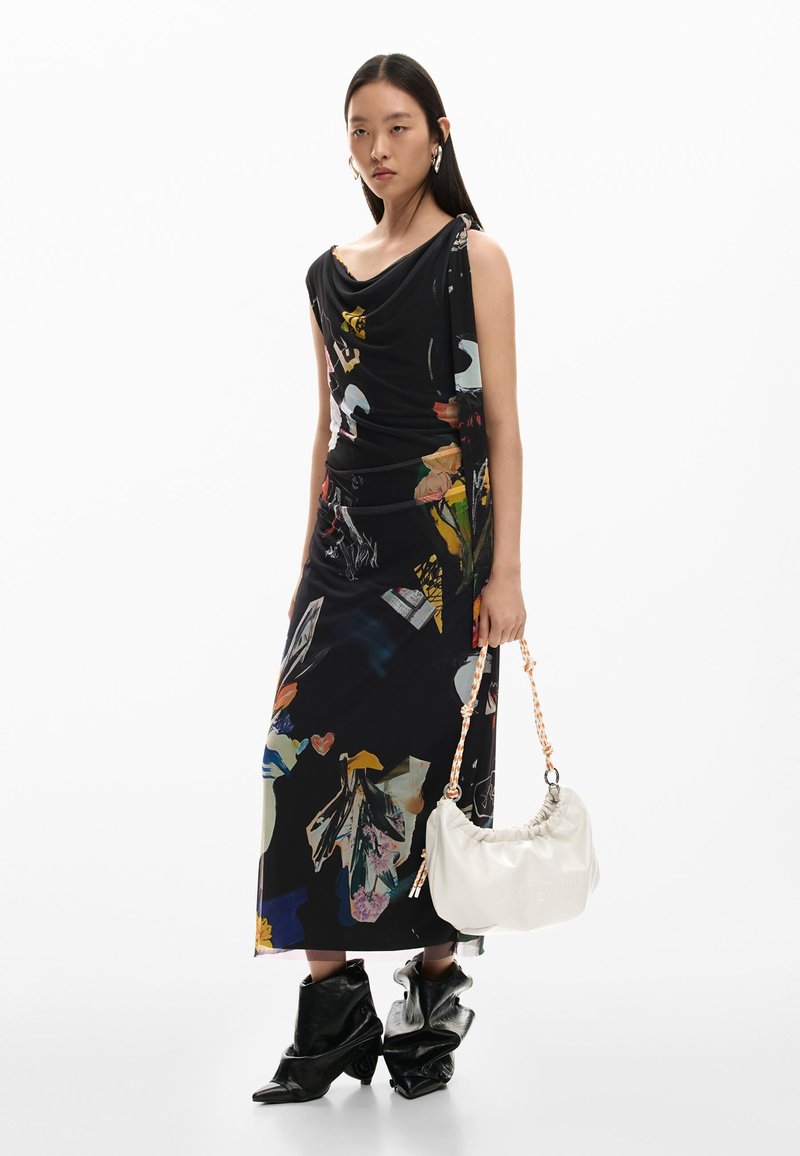 Femme portant une robe noire à imprimé abstrait, des bottes noires décontractées, des boucles d'oreilles créoles dorées, tenant un sac à main blanc froncé avec une sangle orange et blanche.