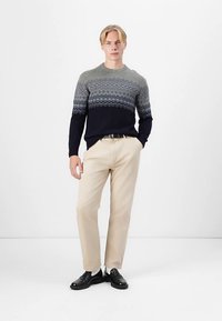 Modře a šedě vzorovaný pletený svetr s vlnovým vzorem, doplněný béžovými kalhotami a černými botami. Jednoduchý střih a hladká textura.