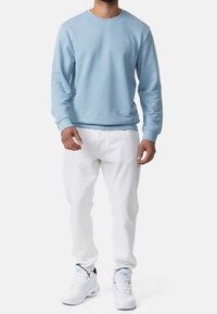 Lichtblauwe sweatshirt met ronde hals en geribbelde manchetten, gecombineerd met witte broek en slanke witte sneakers met blauwe accenten.
