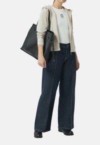 Schwarze Ledertasche mit glatter Textur, getragen zu einem beigen Kapuzensweatshirt mit Reißverschluss, einem weißen, gerippten Tanktop und dunkelblauen, weiten Jeans.