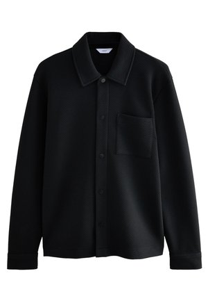 Veste-chemise noire texturée à manches longues avec col, boutons-pression à l'avant et poche poitrine, présentée sur fond blanc.