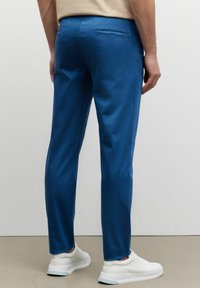 Modré bavlněné kalhoty s hladkou texturou, slim fit, a jednou zadní kapsou, doplněné bílými teniskami.