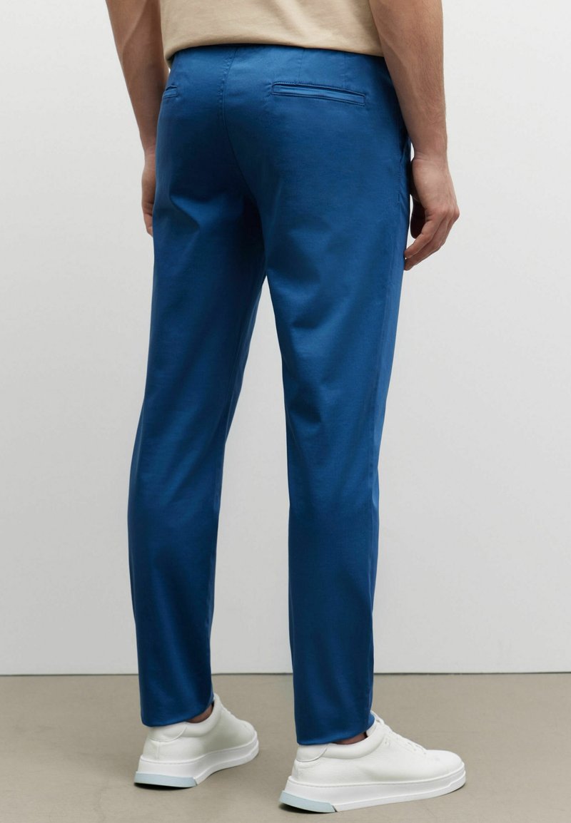 Modré bavlněné kalhoty s hladkou texturou, slim fit, a jednou zadní kapsou, doplněné bílými teniskami.