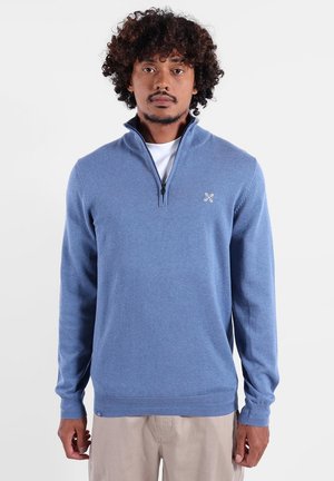 Pull zippé bleu clair en matière douce, doté d'un col haut, de manches longues et d'un petit logo sur la poitrine.