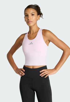 Vaaleanpunainen lyhyt urheilutankkitoppi pyöreällä pääntiellä ja harmaalla logokuvioinnilla, yhdistetty korkeavyötäröisiin mustiin leggingsseihin. Sileä pinta.