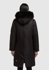 Musta parkatakki turkiksella vuoratulla hupulla, pitkä malli, sileä pinta ja napsautettavat sulkimet alareunassa. Sivutaskut mukana.