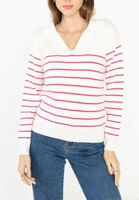 Un pull blanc avec des rayures horizontales roses, en V, et un col. Remarque : poignets et ourlet côtelés. Associé à un jean bleu.