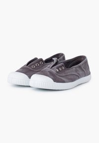 Zapatillas tipo slip-on de lienzo gris con suelas de goma blanca, punta redonda y detalle de ojales en el cordón. Textura suave con un diseño minimalista.