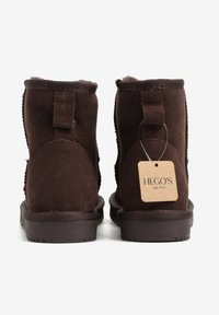 Brązowe zamszowe botki za kostkę o gładkiej fakturze, z dwoma tylnymi pętelkami i zawieszką z napisem "HEGO'S MILANO". Płaskie gumowe podeszwy.