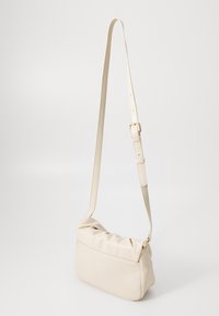 Beige neplederen schoudertas met verstelbare riem, zachte geplooide bovenkant en een gladde textuur. Voorzien van een ritssluiting en subtiele stiksels.