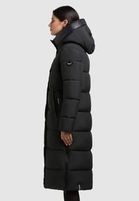 Manteau noir rembourré avec capuche, doté d'une fermeture éclair à l'avant et de poches latérales. Fabriqué en matériau isolant avec un motif matelassé.