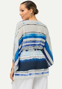 Top in stile kimono trasparente con strisce orizzontali blu e nere. Presenta una vita stretta e maniche ampie, realizzato in tessuto leggero.