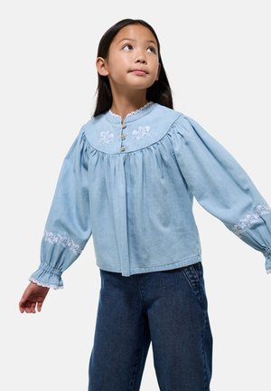Blouse en denim bleu clair avec des accents floraux brodés, corsage froncé et longues manches bouffantes, dotée d'une fermeture à boutons et d'un bord en dentelle.