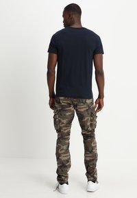 Marineblauw katoen t-shirt en groene camouflage cargo pants met zijzakken. De outfit heeft een ontspannen pasvorm en witte sneakers.