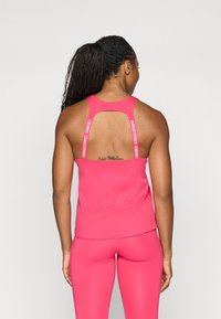 Ružičasti sportski top s dizajnom racerback, koji ima izrezane detalje i bijelo "NIKE PRO" logo na naramenicama. Glatka, rastezljiva tkanina.