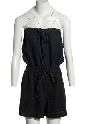 Combinaison noire bustier avec un haut élastique froncé et une ceinture nouée à la taille sur un torse de mannequin blanc.