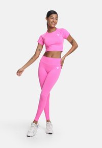 Prikladna ružičasta kratka majica i tajice od rastezljivog materijala, s glatkom teksturom i bijelim logotipom. Obuća su bijele atletske cipele.