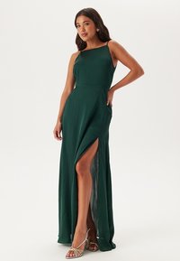 Abito verde lungo fino al pavimento con scollatura dritta e spacchi alti fino alla coscia. Realizzato in un tessuto morbido, presenta spalline sottili e una vita aderente.