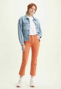 Giacca di jeans azzurra chiara, t-shirt bianca, pantaloni arancioni cropped e sneakers bianche con accenti arancioni. Design classico e vestibilità casual.