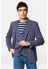 Marynarski i biały żakiet w wzór houndstooth z podwójnym zapięciem, zestawiony z niebieską i białą koszulą w paski oraz dżinsami.