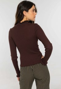 Top marrón de manga larga con textura acanalada y escote con volantes, combinado con pantalones de talle alto con estampado a cuadros. Diseño sencillo y ajustado.