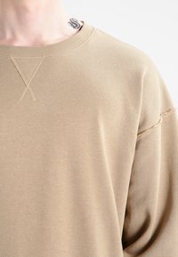 Beige színű pulóver kerek nyakkivágással, bordás gallérral és látható varrás részletekkel. Puha tapintású, laza szabású, esősen eső vállakkal.
