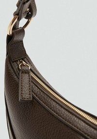 Brązowa skórzana torba na ramię o teksturowanej powierzchni, z detalem złotego zamka błyskawicznego i usztywnionym kształtem. W zestawie regulowany pasek.