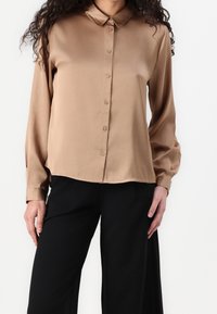 Satin, beige knapp-up skjorta med krage, långa ärmar och rak skärning. Har en slät yta och subtil lyster. Matchas med svarta byxor.