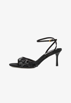 Sandalia de tacón stiletto negra con punta abierta, con tira en el tobillo y grandes lentejuelas negras brillantes en la tira frontal, sobre fondo blanco.