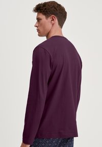 Langarm T-shirt in donkerpaarse katoen. Rond de hals en een relaxte pasvorm. Heeft minimale stiksels en geen zichtbare logo's of patronen.