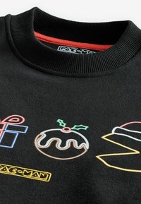 Suéter negro con cuello redondo acanalado, que presenta coloridos diseños bordados, incluyendo un regalo, un pudín y un motivo de Pac-Man.