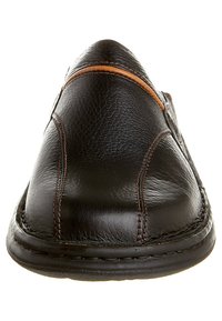 Zapato negro de cuero tipo slip-on con un acabado texturizado, con costuras marrones y un diseño superior liso. Suela plana visible.