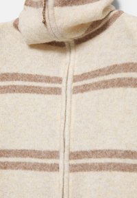Sweter z wełny w kolorze kremowym i beżowym, z suwakem z przodu oraz dwiema poziomymi brązowymi paskami na klatce piersiowej.