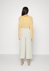 Top a maniche lunghe a righe arancione e bianche, abbinato a pantaloni palazzo beige chiaro. Tacchi chunky color cammello completano l'outfit.