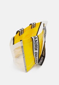Borsa a spalla gialla con fondo bianco traslucido, robuste maniglie a strisce nere e bianche, forma rettangolare e materiale texturizzato e resistente.