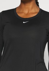 Frau trägt ein schwarzes Nike-Shirt mit langen Ärmeln, auf dem sich das weiße Nike-Swoosh-Logo zentriert unter dem Kragen befindet.