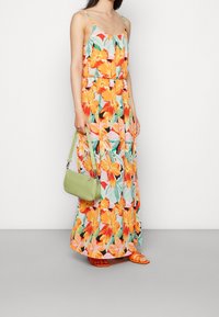 Maxi-jurk met een bloemenpatroon met oranje, roze en groene tinten; lichtgewicht stof, spaghettibandjes en een ontspannen pasvorm. Accessoire: groene handtas.