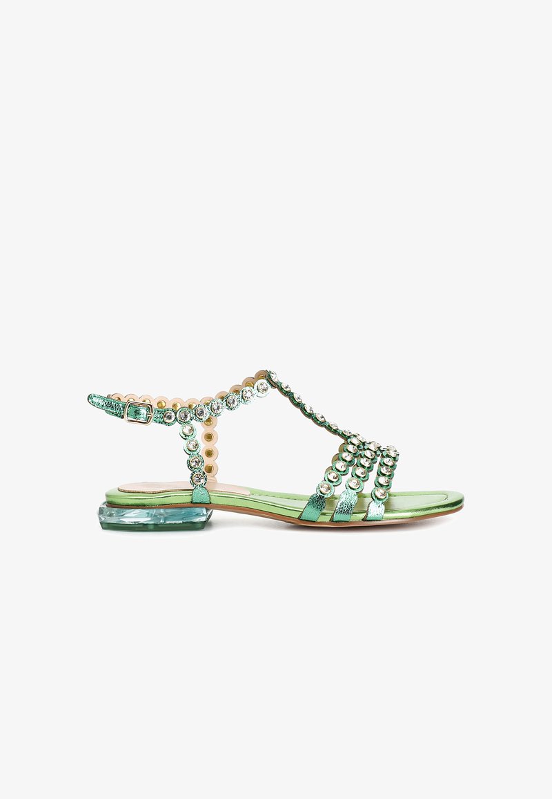 Green sandal with a low block heel. Features metallic straps, round decorative beads, and a textured ankle strap with a buckle.