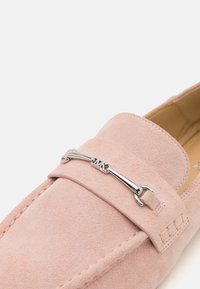 Light pink suede loafers with a metal accent featuring the initials "MK" on the front, showcasing a flat profile and stitched details.