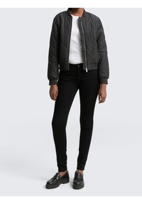 Czarna pikowana kurtka bomber z prążkowanymi mankietami i kołnierzem, zestawiona z dopasowanymi czarnymi dżinsami i masywnymi czarnymi mokasynami. Pod spodem prosty biały top.