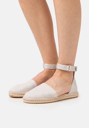 Espadrilles gris claro con suela de yute trenzado, lados abiertos y correa de tobillo ajustable. Presentan una textura suave y un diseño simple.