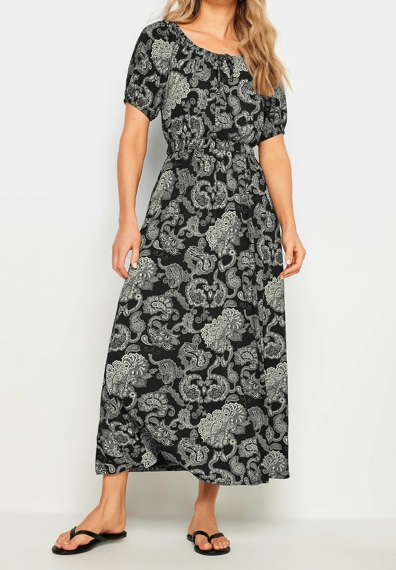 Femme portant une robe midi à motif paisley noir et blanc, manches courtes et taille élastique, associée à des sandales flip-flop noires.