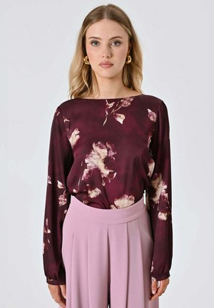 Blusa a maniche lunghe in bordeaux con stampa floreale, abbinata a pantaloni plissettati rosa chiaro. Tessuto liscio e vestibilità comoda.