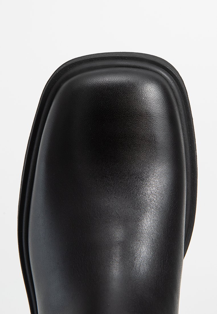 Zwarte leren laars met een gladde, ronde neus en een subtiele glans. Beschikt over een versterkte naad en een stevige zool.