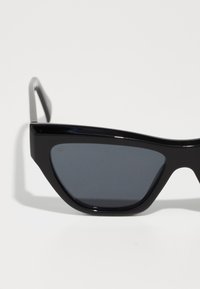 Ochelari de soare negri, în formă de ochi de pisică, cu lentile de un gri nuanțat. Fabricati din plastic lucios, având un design ascuțit și un cadru subțire de culoare neagră.