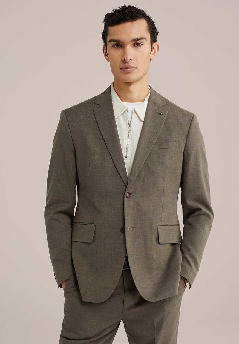 Tume oliivroheline ülikondjakk, millel on kaks nööpi, sisselõigatud krae ja eesmine taskud. Seljas helebeeži värvi tõmblukuga särk. Sile tekstuur.